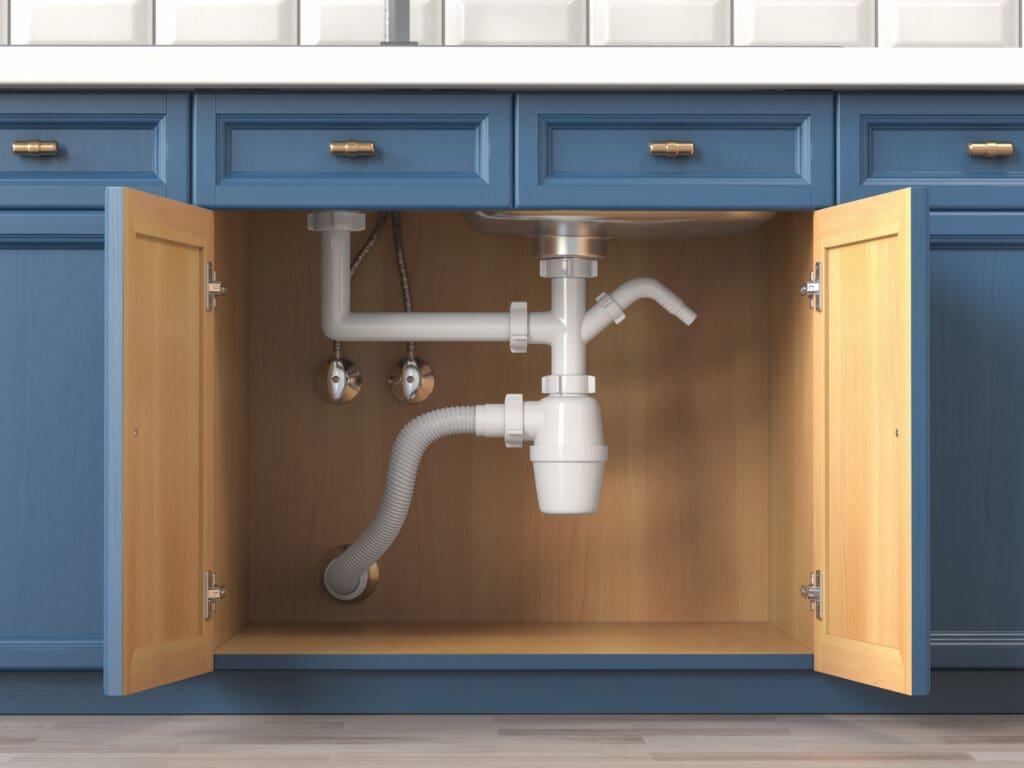 Open cabinet doors reveal plumbing under a kitchen sink, featuring blue cabinetry and white pipes. The countertop is white, contrasting with the warm wood interior of the cabinet.