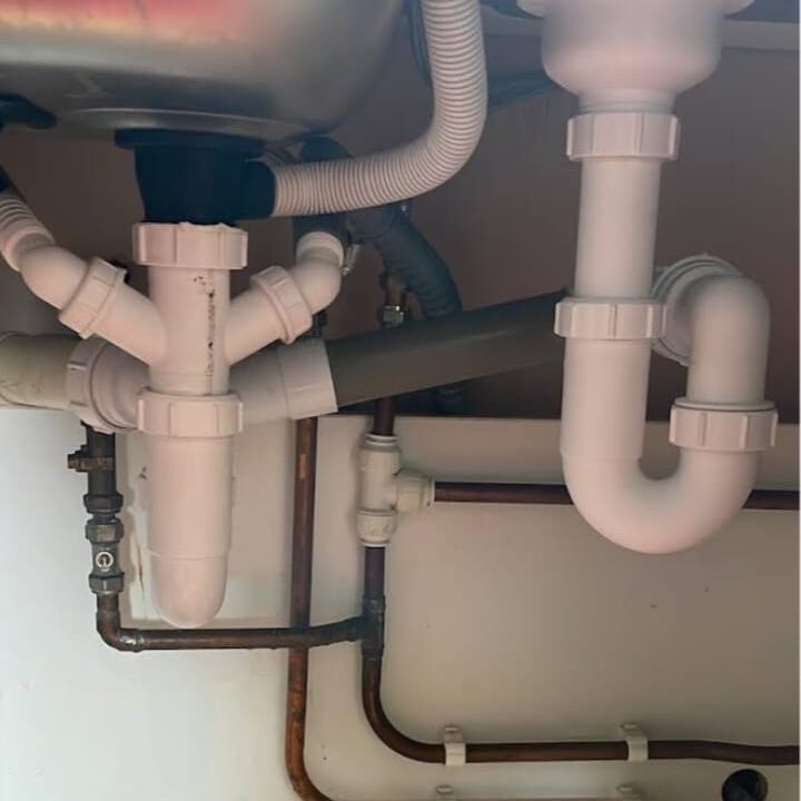 View of plumbing under a sink, showing white plastic pipes and gray conduits connected to metal pipes.